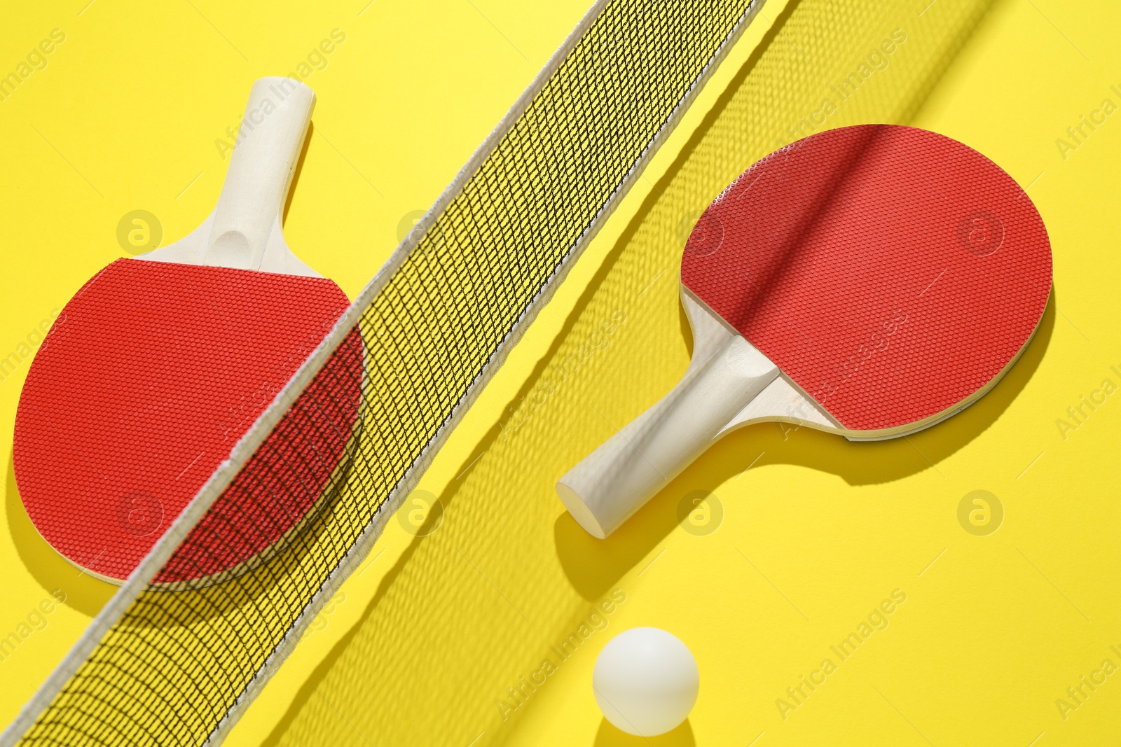 Ping pong rackets, ball and net on yellow background Photo of Ping pong rackets, ball and net on yellow background