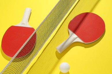 Photo of Ping pong rackets, ball and net on yellow background