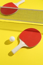 Photo of Ping pong rackets, ball and net on yellow background