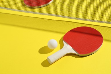 Photo of Ping pong racket, ball and net on yellow background