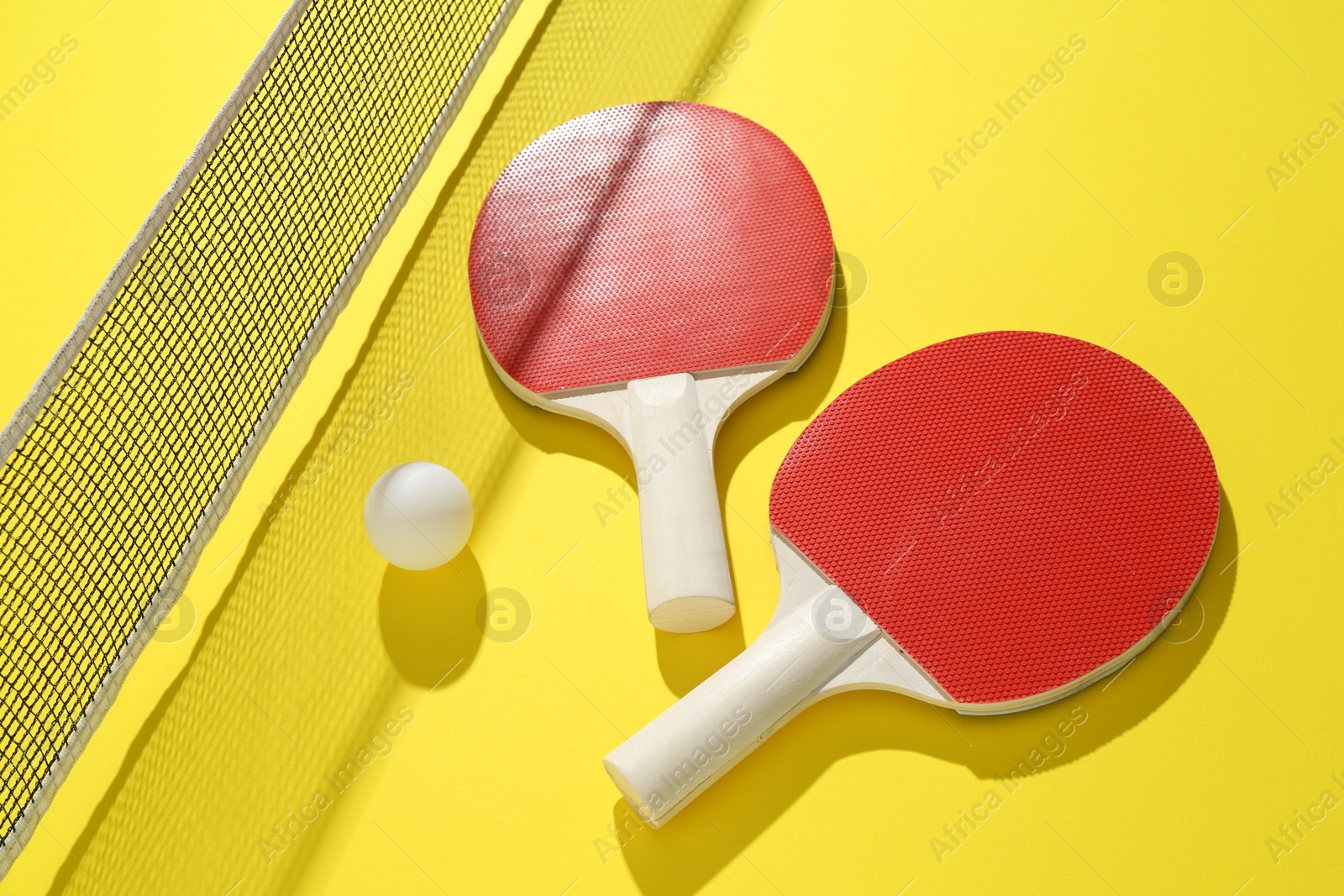 Ping pong rackets, ball and net on yellow background Photo of Ping pong rackets, ball and net on yellow background