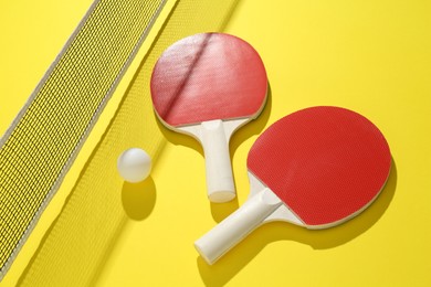 Photo of Ping pong rackets, ball and net on yellow background