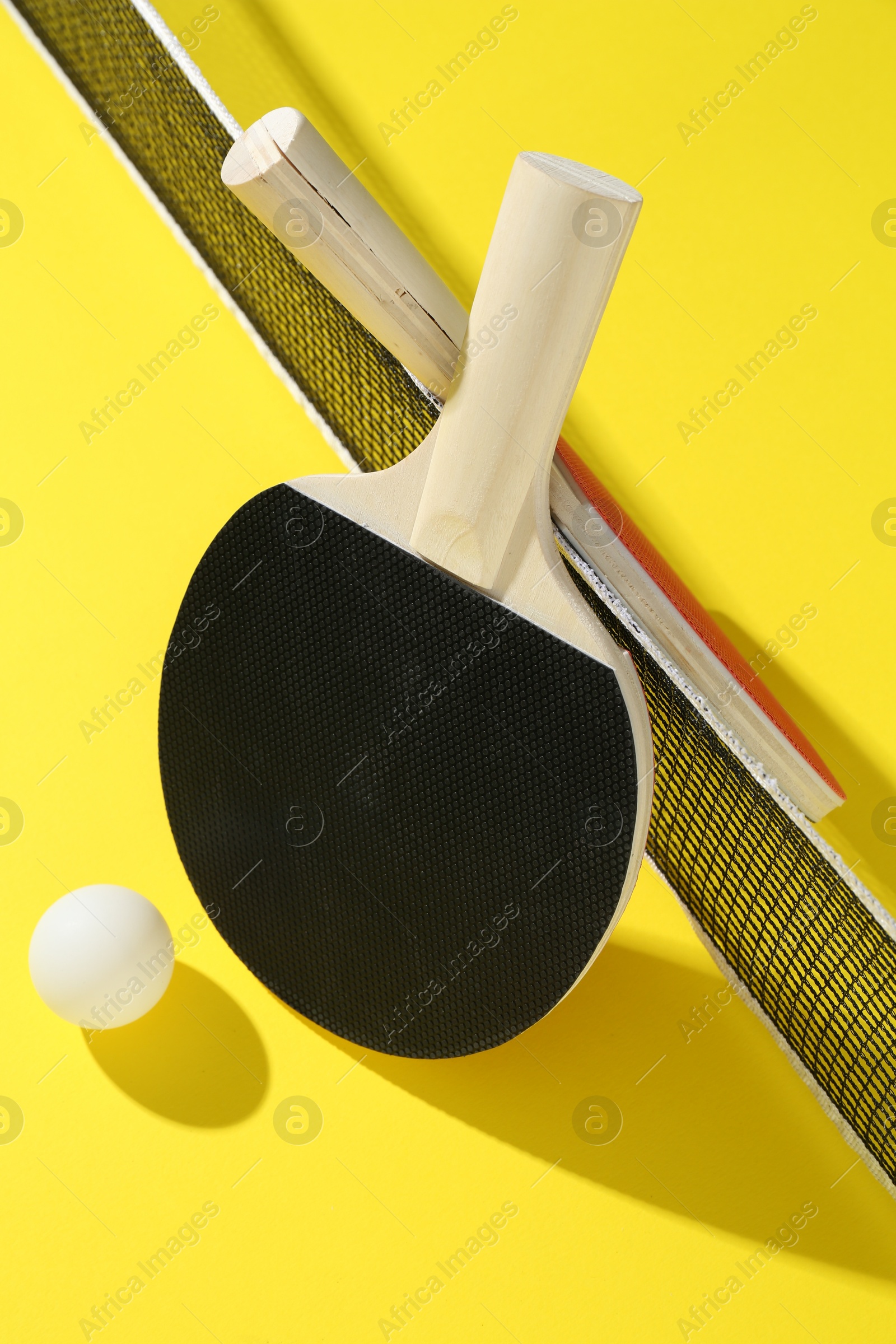 Ping pong rackets, ball and net on yellow background Photo of Ping pong rackets, ball and net on yellow background