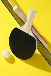 Photo of Ping pong rackets, ball and net on yellow background
