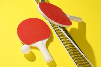Photo of Ping pong rackets, ball and net on yellow background