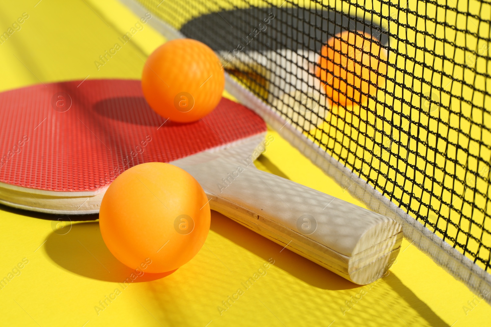 Ping pong rackets, balls and net on yellow background, closeup Photo of Ping pong rackets, balls and net on yellow background, closeup
