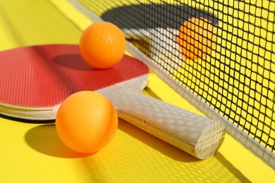 Photo of Ping pong rackets, balls and net on yellow background, closeup