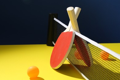 Photo of Ping pong rackets and balls on yellow table. Space for text