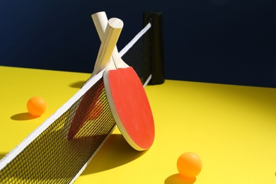 Photo of Ping pong rackets and balls on yellow table. Space for text