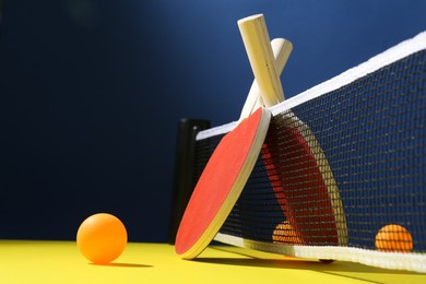 Photo of Ping pong rackets and balls on yellow table. Space for text