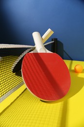 Photo of Ping pong rackets and ball on yellow table
