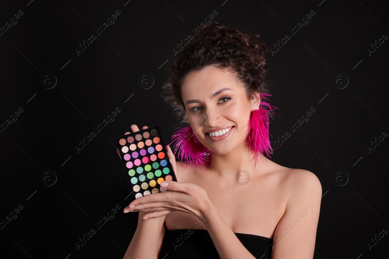 Smiling woman with bright eyeshadow palette on black background Photo of Smiling woman with bright eyeshadow palette on black background
