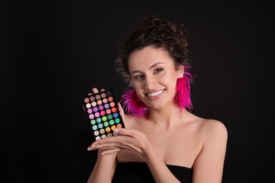 Photo of Smiling woman with bright eyeshadow palette on black background