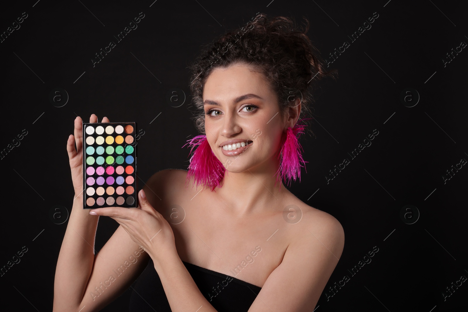Smiling woman with bright eyeshadow palette on black background Photo of Smiling woman with bright eyeshadow palette on black background