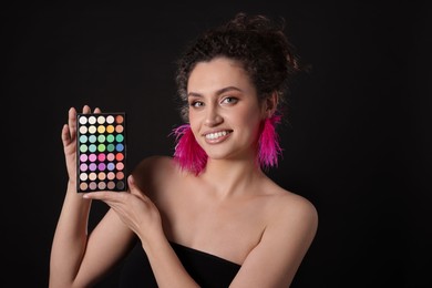 Photo of Smiling woman with bright eyeshadow palette on black background