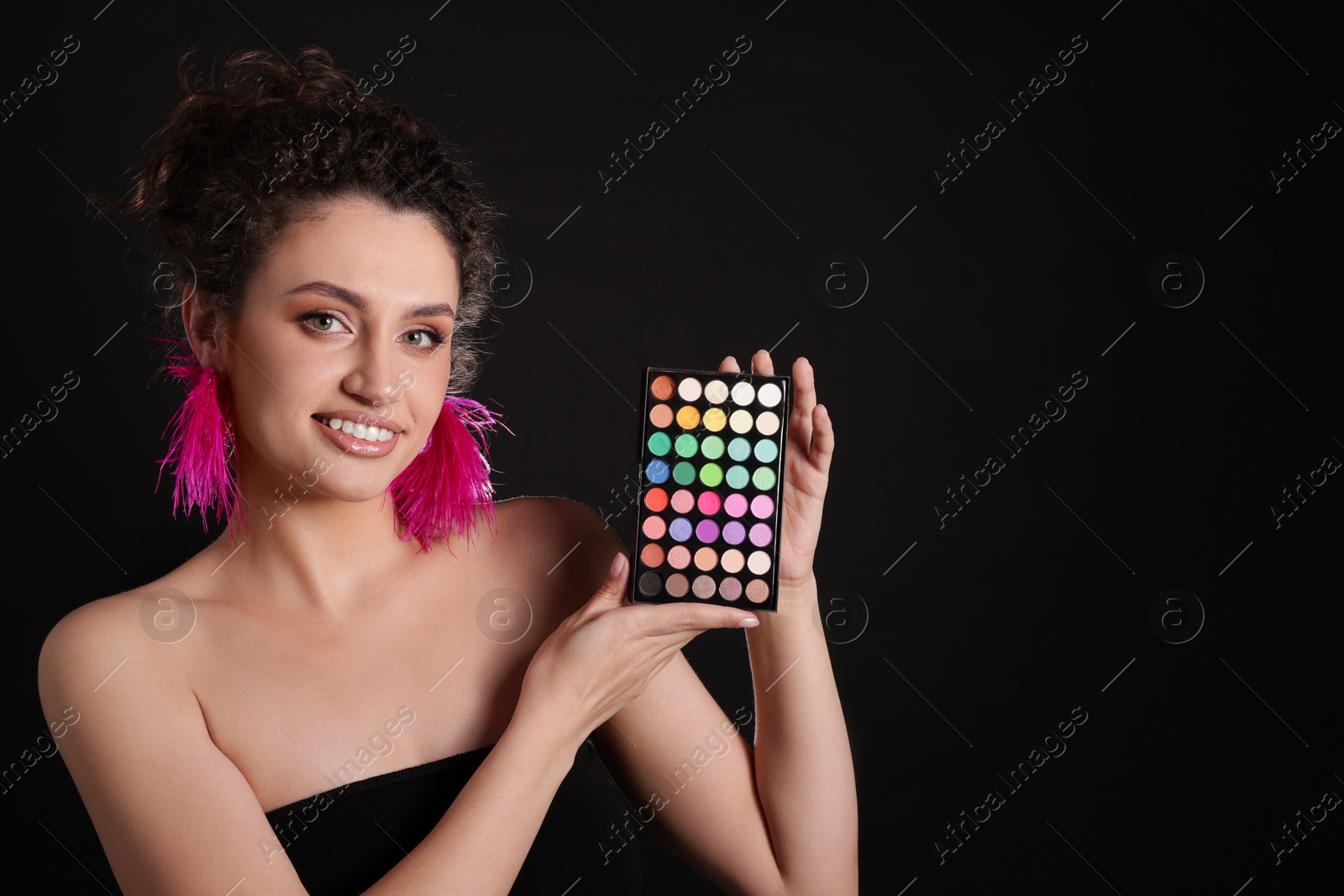 Smiling woman with bright eyeshadow palette on black background. Space for text Photo of Smiling woman with bright eyeshadow palette on black background. Space for text
