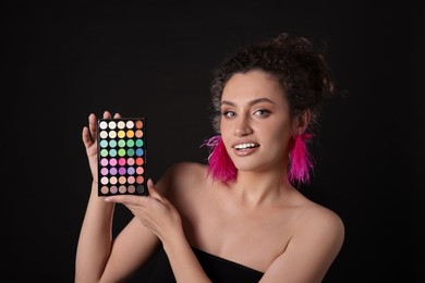 Photo of Woman with bright eyeshadow palette on black background