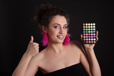 Photo of Woman with bright eyeshadow palette showing thumbs up on black background