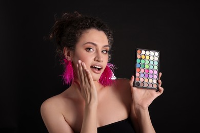 Photo of Surprised woman with bright eyeshadow palette on black background