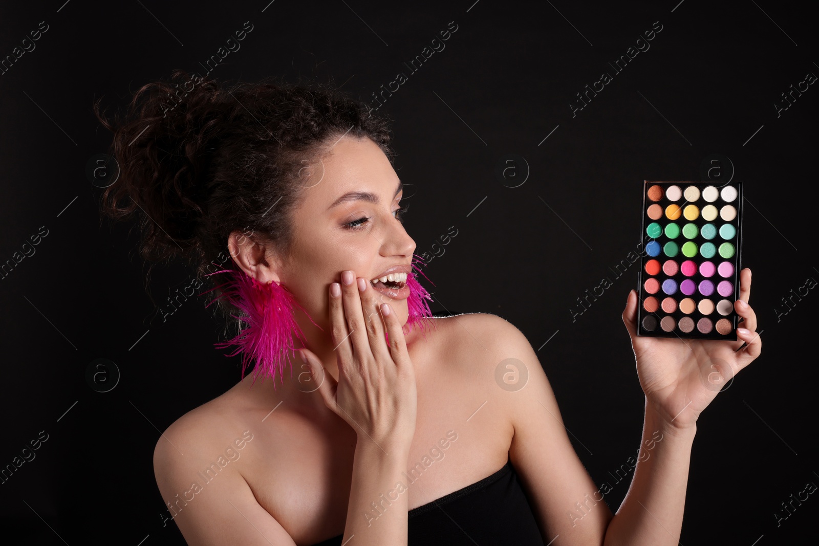 Surprised woman with bright eyeshadow palette on black background Photo of Surprised woman with bright eyeshadow palette on black background