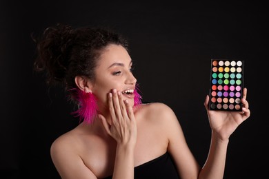 Photo of Surprised woman with bright eyeshadow palette on black background