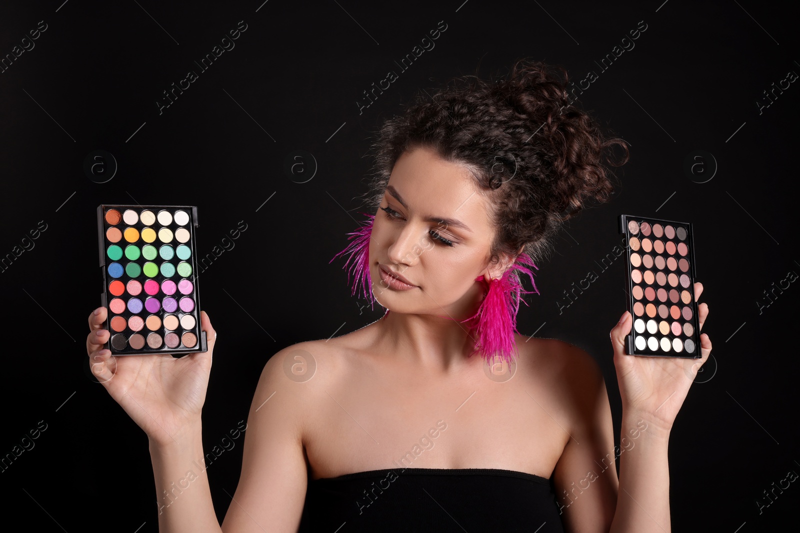 Woman with eyeshadow palettes on black background Photo of Woman with eyeshadow palettes on black background