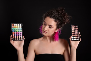 Photo of Woman with eyeshadow palettes on black background