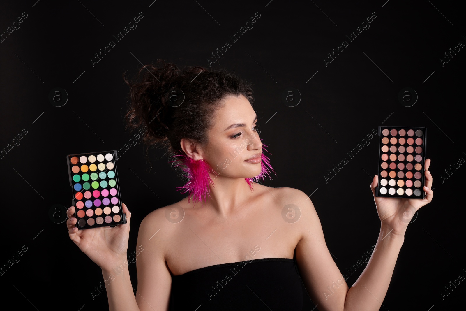 Woman with eyeshadow palettes on black background Photo of Woman with eyeshadow palettes on black background