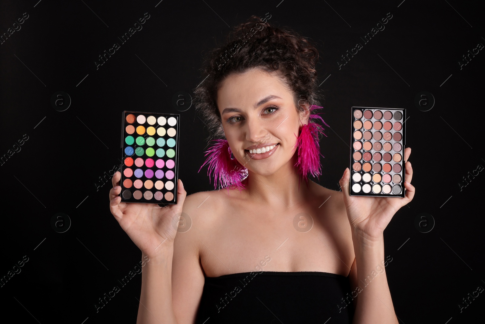 Smiling woman with eyeshadow palettes on black background Photo of Smiling woman with eyeshadow palettes on black background