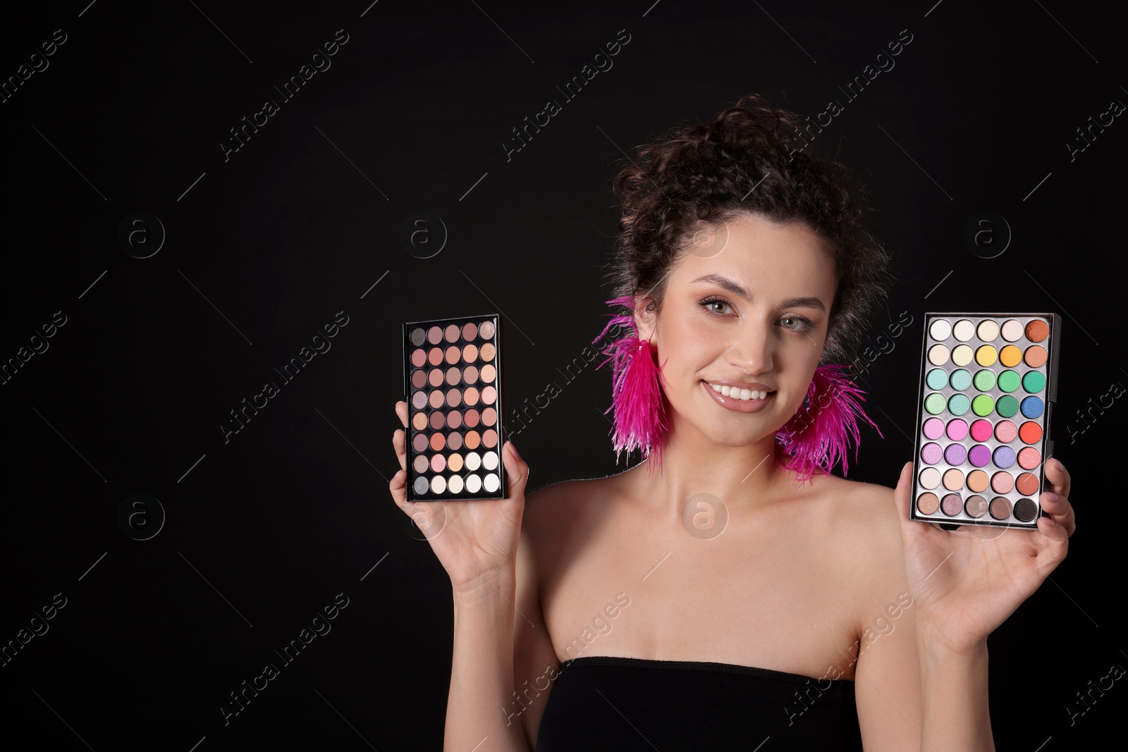 Smiling woman with eyeshadow palettes on black background. Space for text Photo of Smiling woman with eyeshadow palettes on black background. Space for text
