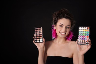 Photo of Smiling woman with eyeshadow palettes on black background. Space for text