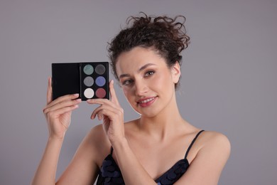 Photo of Smiling woman with eyeshadow palette on grey background