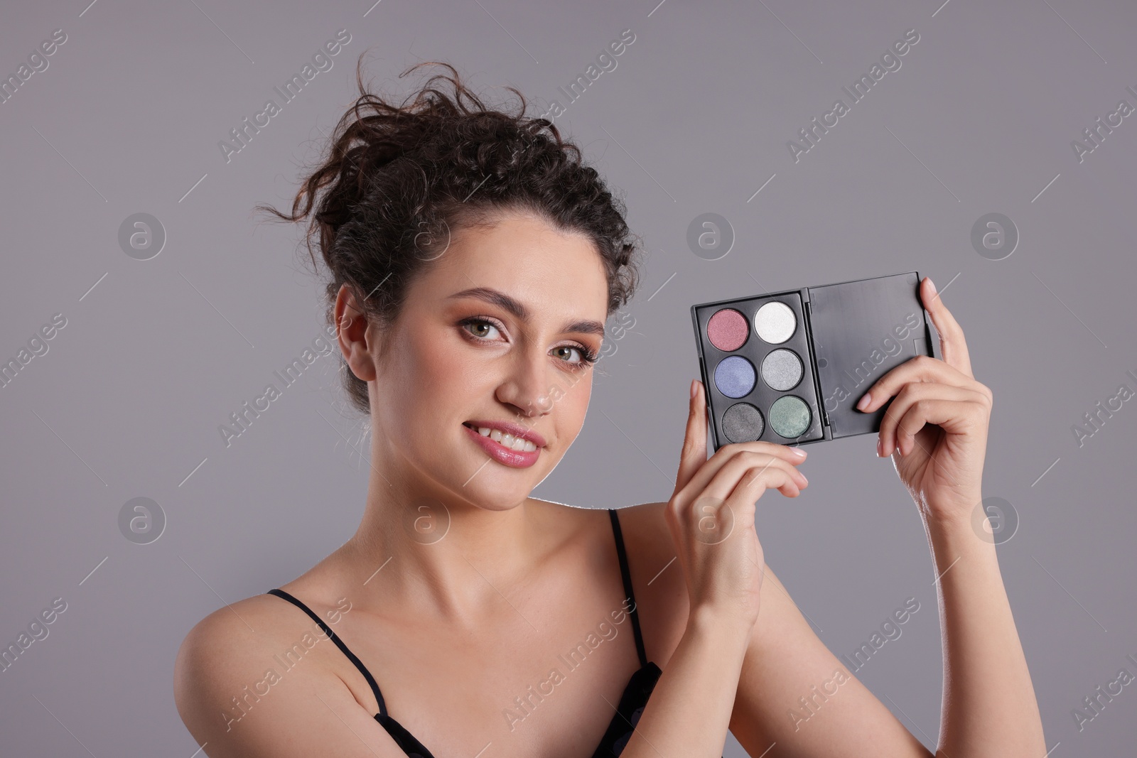 Smiling woman with eyeshadow palette on grey background Photo of Smiling woman with eyeshadow palette on grey background