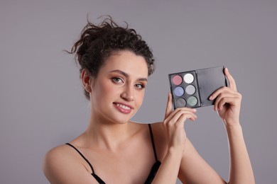 Photo of Smiling woman with eyeshadow palette on grey background