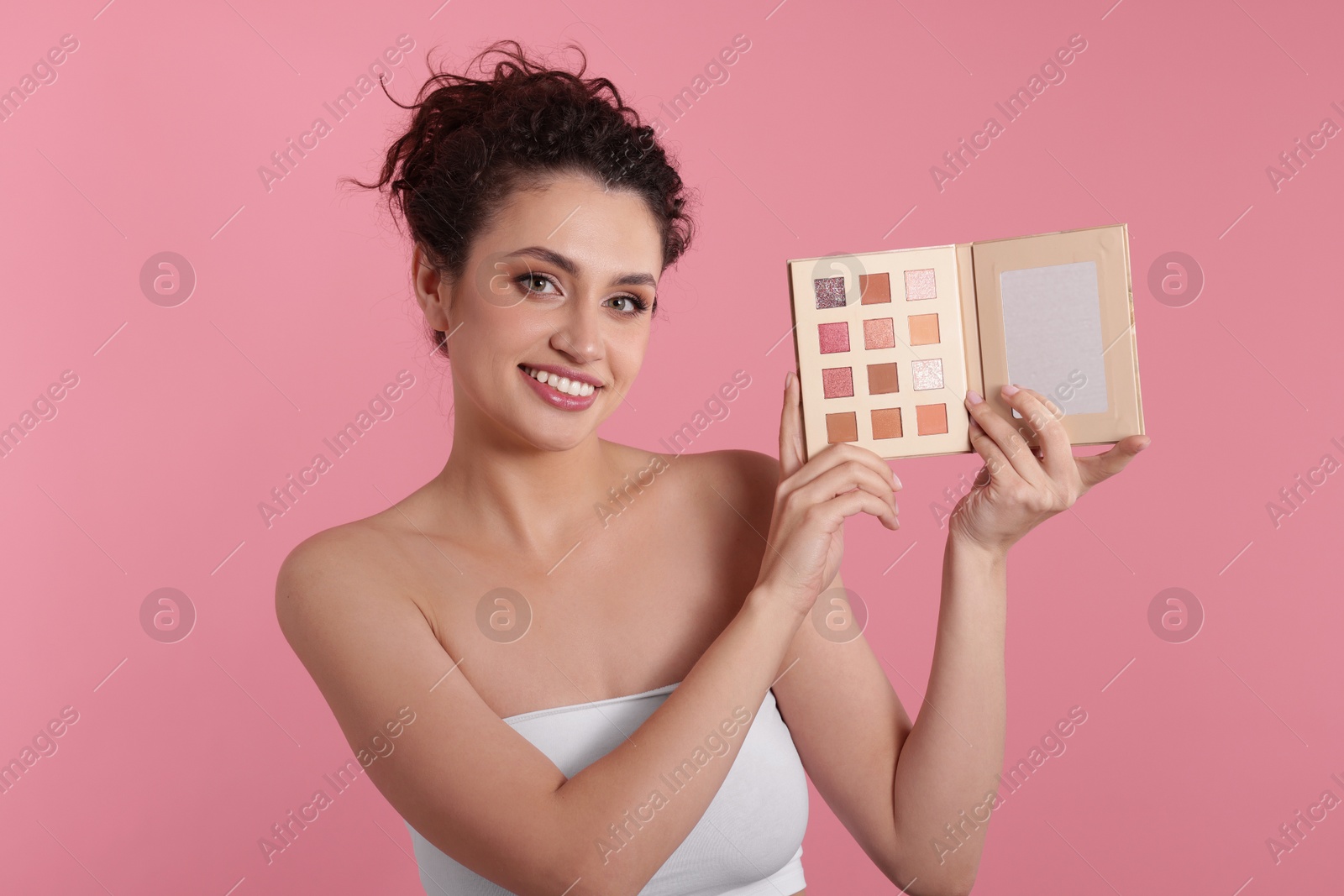 Smiling woman with eyeshadow palette on pink background Photo of Smiling woman with eyeshadow palette on pink background