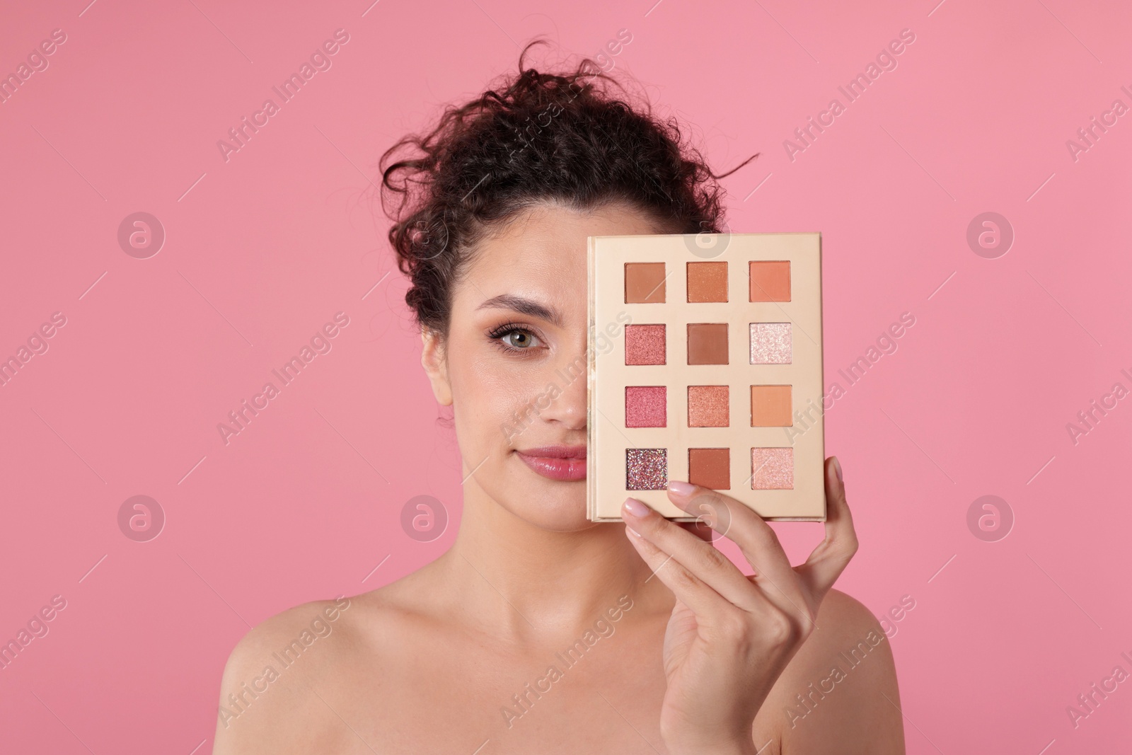Woman covering eye with eyeshadow palette on pink background Photo of Woman covering eye with eyeshadow palette on pink background