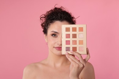Photo of Woman covering eye with eyeshadow palette on pink background