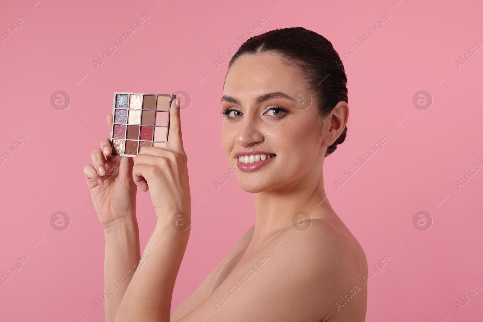 Smiling woman with eyeshadow palette on pink background Photo of Smiling woman with eyeshadow palette on pink background