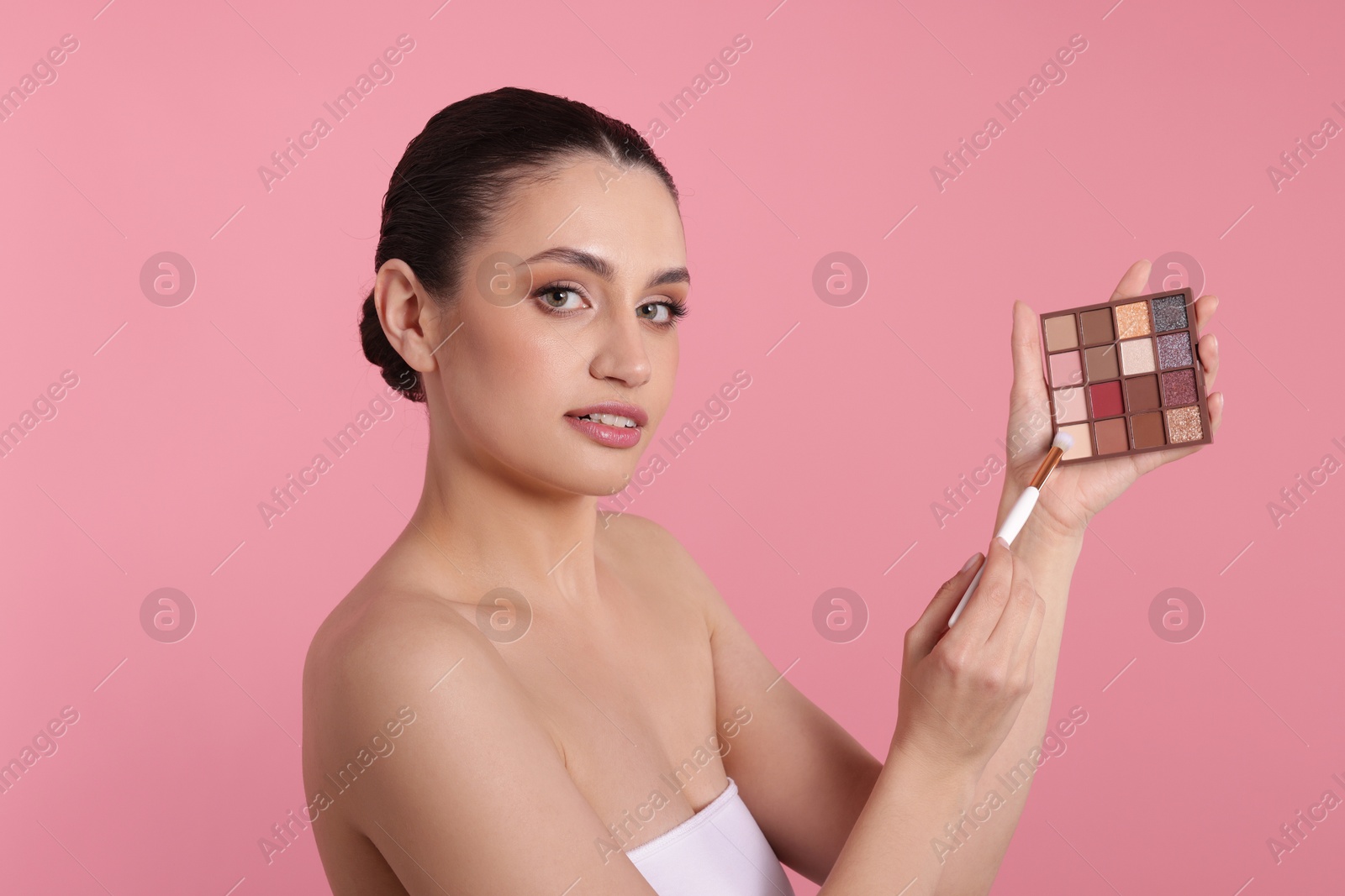 Woman with eyeshadow palette and brush on pink background Photo of Woman with eyeshadow palette and brush on pink background