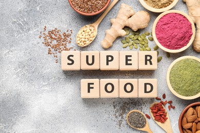 Photo of Wooden cubes with words Super Food, products and supplements on grey textured table, flat lay. Space for text