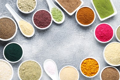 Photo of Frame of different superfood powders on grey textured table, flat lay. Space for text