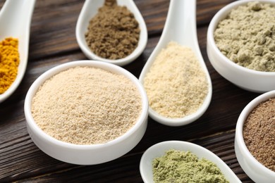 Photo of Different superfood powders in spoons and bowls on wooden table, closeup
