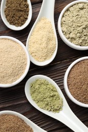 Photo of Different superfood powders in spoons and bowls on wooden table, flat lay