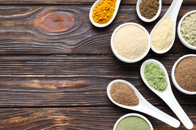 Photo of Different superfood powders in spoons and bowls on wooden table, flat lay. Space for text