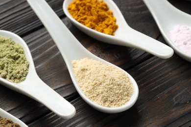 Photo of Different superfood powders in spoons on wooden table, closeup
