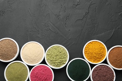 Photo of Different superfood powders in bowls on dark textured table, flat lay. Space for text