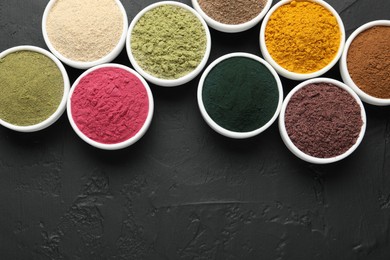 Photo of Different superfood powders in bowls on dark textured table, flat lay. Space for text