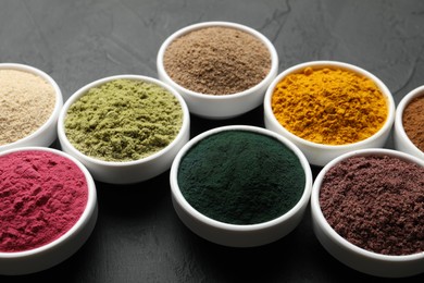 Photo of Different superfood powders in bowls on dark textured table, closeup