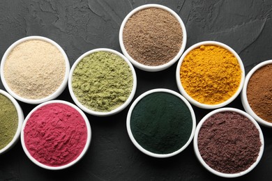 Photo of Different superfood powders in bowls on dark textured table, flat lay