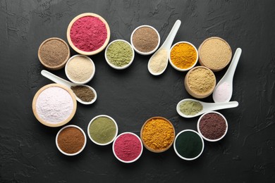 Photo of Frame of different superfood powders in bowls and spoons on dark textured table, flat lay. Space for text